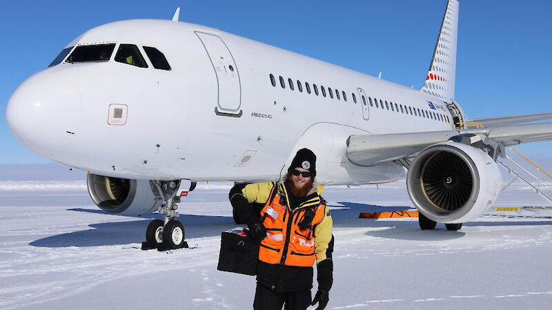 A man carrying a bag of vaccines smiles in front of a plane