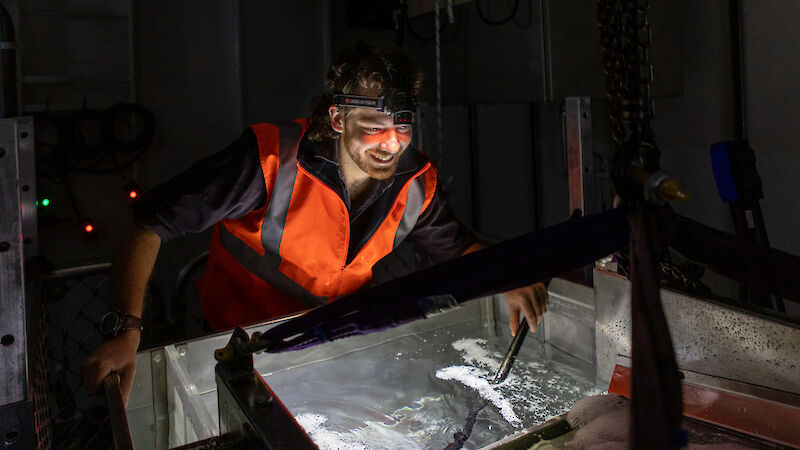 A scientist leans over a tank of water, surrounded by equipment.