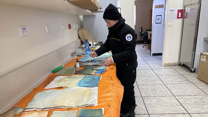 A woman paints blue scenes on paper in a science lab