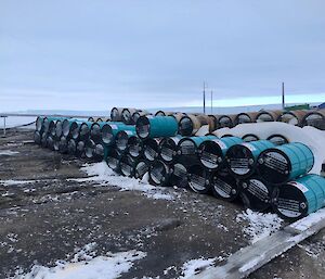 A stack of 36 blue fuel drums, three high, lies across rocky snow covered ground