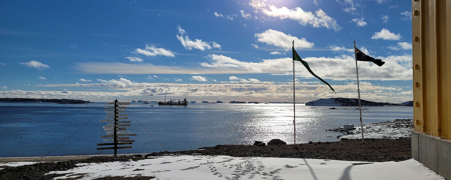 An ocean view with blue sky, snow on the ground and some flags