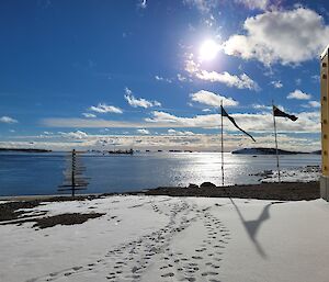 An ocean view with blue sky, snow on the ground and some flags