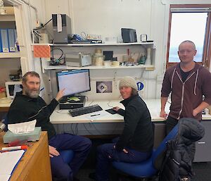 A group of three people sit around a desk