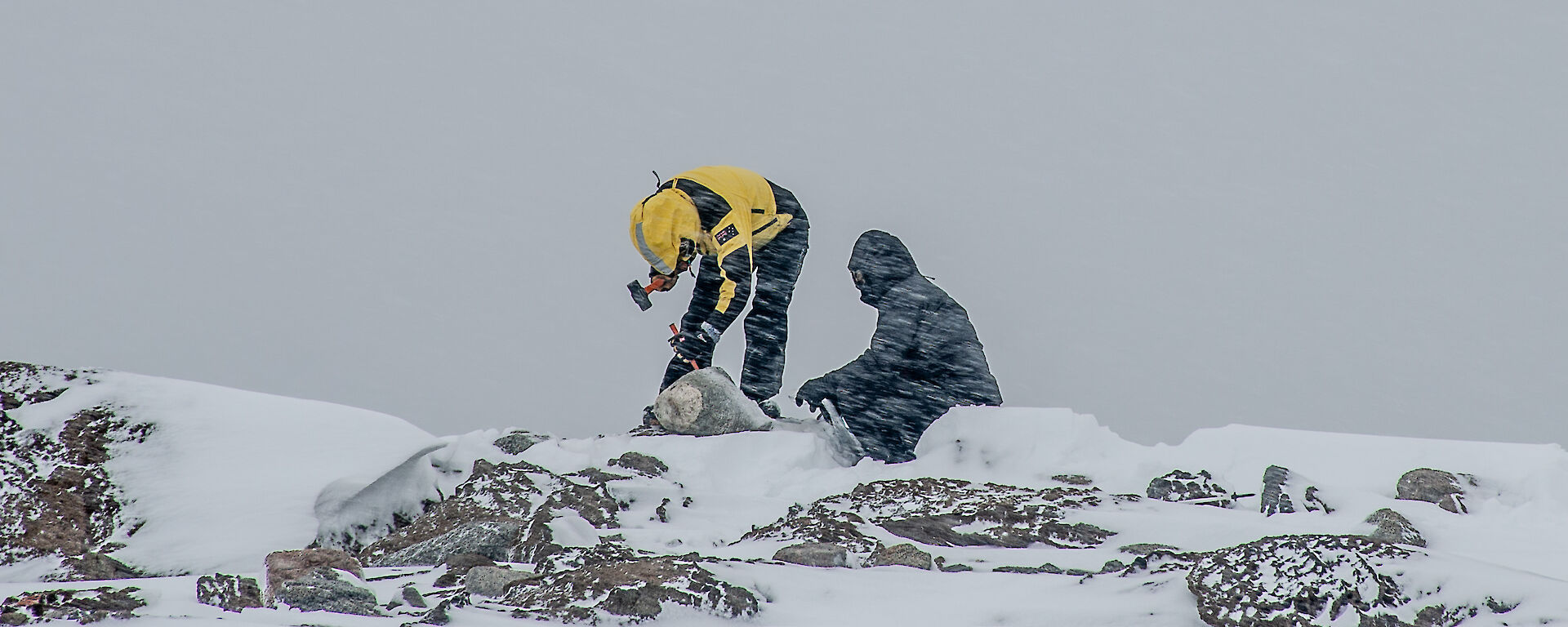 Two people chisel at rocks in the snow