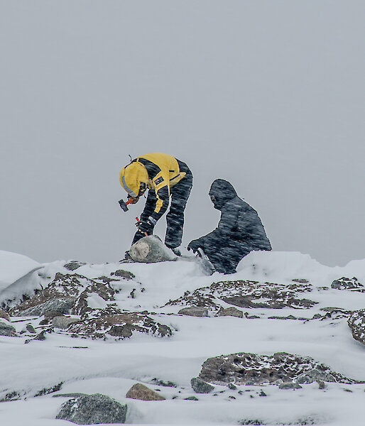 Two people chisel at rocks in the snow