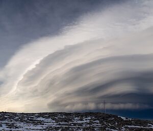 A cloud formation reaching a very great height in the sky. It has many wavelike layers, all seeming to converge downward to a point on the horizon