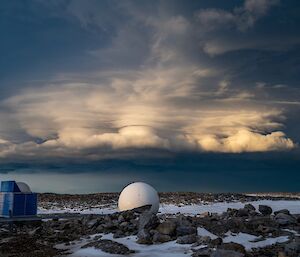 A towering cloud formation in the sky, appearing as flat layers rising from a fluffy base, widening out on top, with a nebulous column rising through the middle