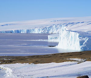 Ice covered bay with ice cliffs rising above and then leading to the ice plateau, blue skies above