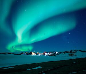 Lights of the station in the distance and overhead a swirling turquoise lights of the aurora