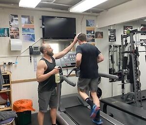 One man wiping anothers brow while running on the treadmill