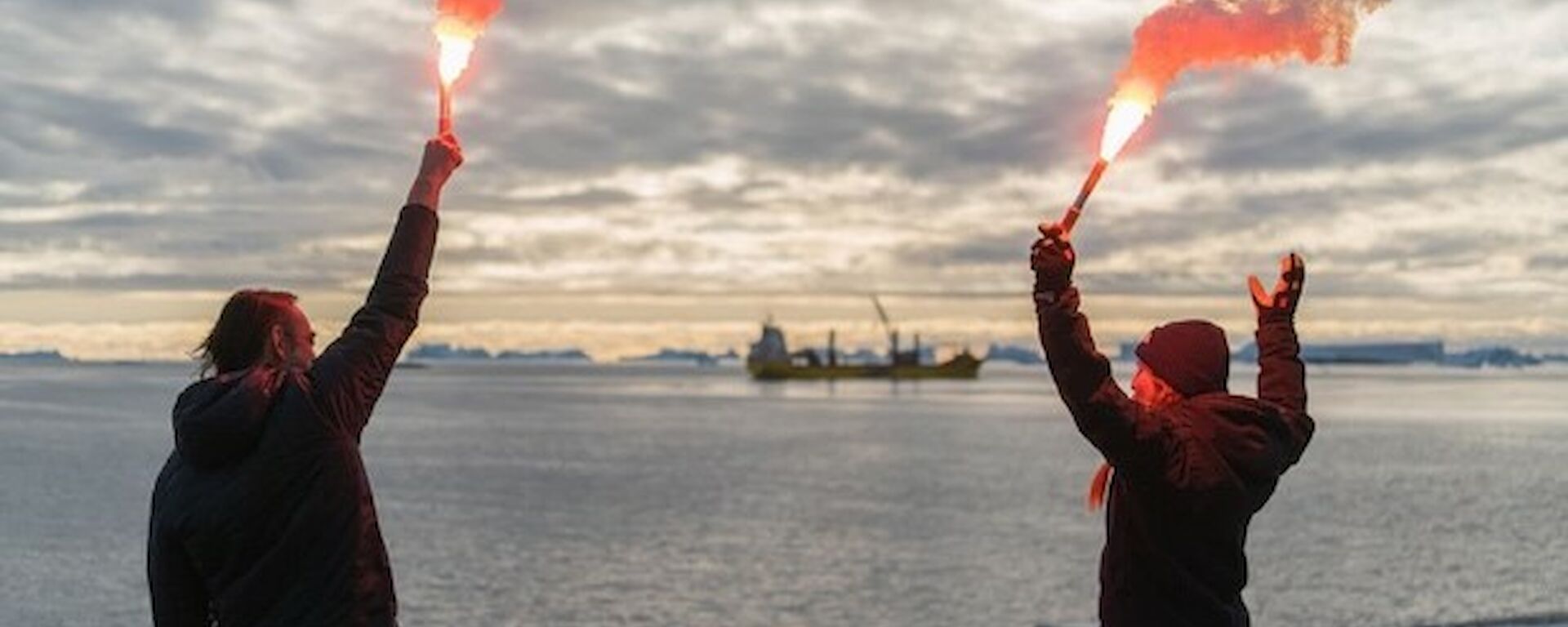 Two people holding flares with a ship departing in the background