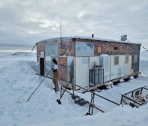 A weatherbeaten hut with a signboard reading "Wilkes Hilton". A large build-up of snow at the entrance has been shovelled through to carve a neat pathway to the hut's door