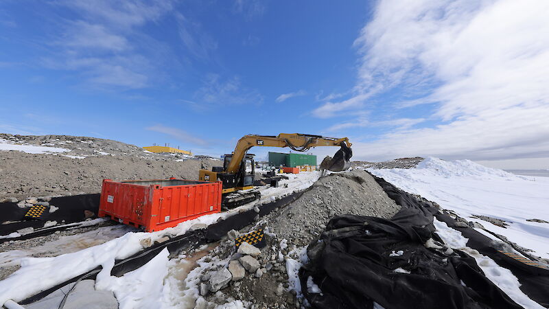 A crane lifts dirt with a blue sky and snow around it