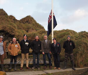 A group of expeditioners stand in front of the Australian flag on a pole