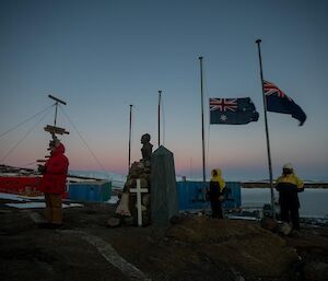 Man stands in front of commemorative cross which is in front of flag poles with flags at half mast