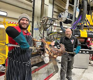 Men hold lamb on spit and smile to camera