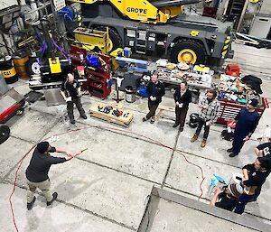 Man throws pennies high in center of rope circle, around the circle the rest of the station population watch in expectation