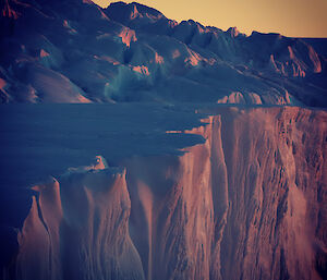 Ice cliffs lit up in pastel blue and pink with a yellow sky