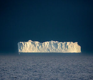 Rectangular shaped iceberg on the ocean with a dark grey sky