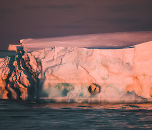 Iceberg with holes in it lit up in pink and orange