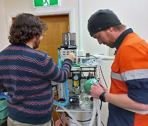 Two people in a medical facility are setting up the ventilator by checking the tubes, wires and dials