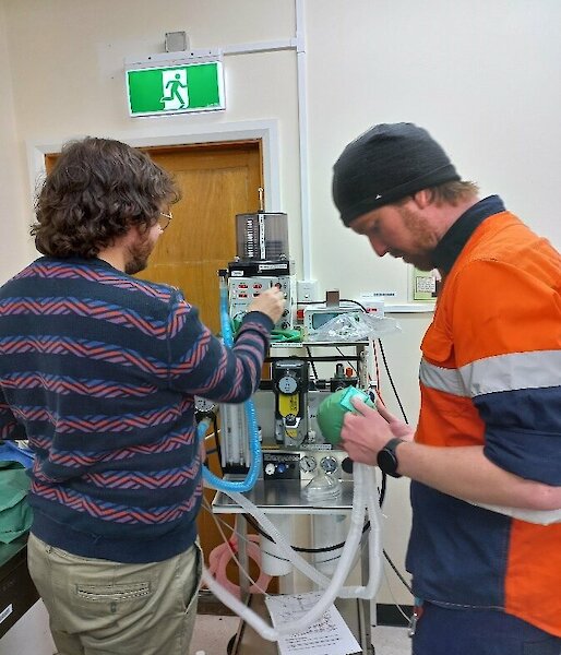 Two people in a medical facility are setting up the ventilator by checking the tubes, wires and dials