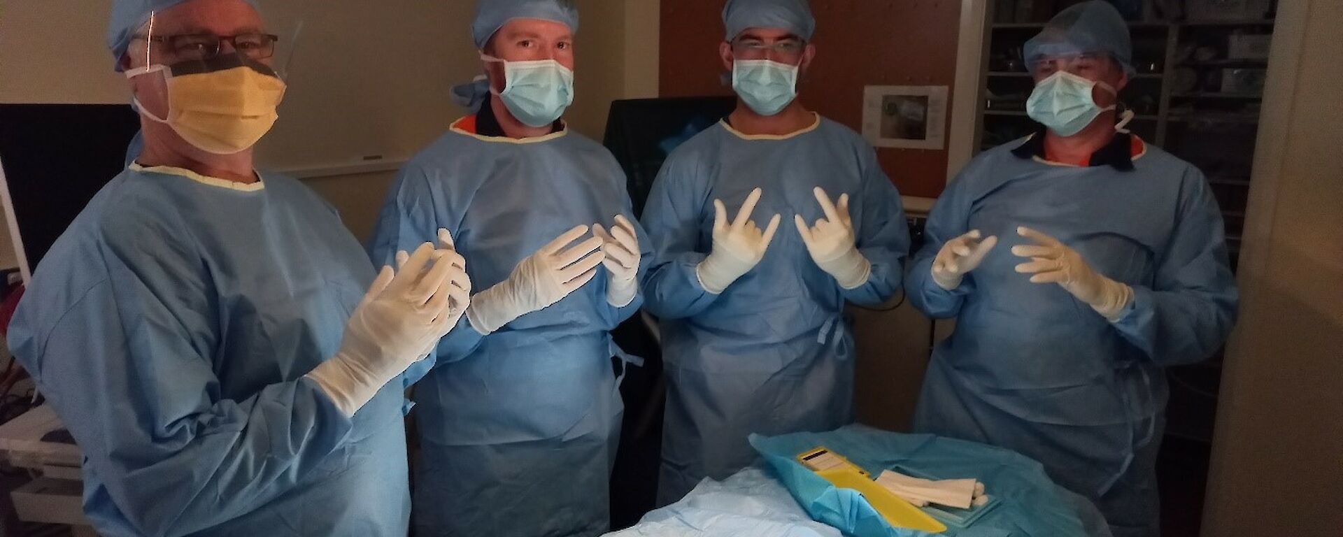 Four people stand in a surgical theatre scrubbed, gowned and ready for surgery
