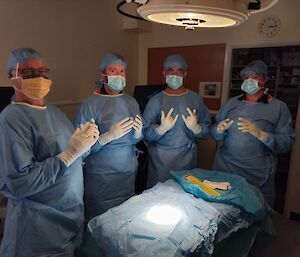 Four people stand in a surgical theatre scrubbed, gowned and ready for surgery