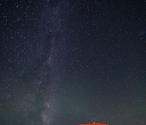 A red shed in foreground with milky way stretching out above in the night sky