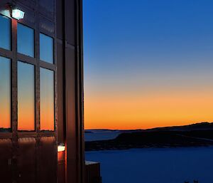 Right side of picture shows sunset over horizon with left side the red shed windows with the sunset reflected