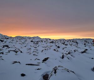 Sun rise behind snow and rocky hills