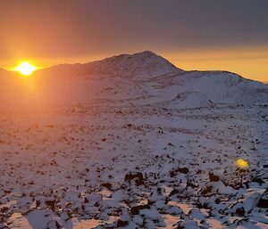 Sun rise behind snow and rocky hills