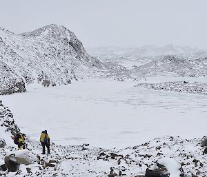 2 expeditioners looking out on snow, ice, frozen lake and rocky hills