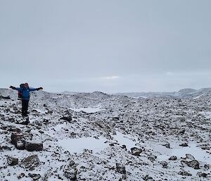 An expeditioner with arms out demonstrating how vast the Vestfold Hills are surrounded by snow and rocks