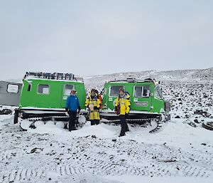 3 men standing in front of a Hagglunds surrounded by rocks and snow