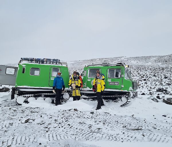 3 men standing in front of a Hagglunds surrounded by rocks and snow