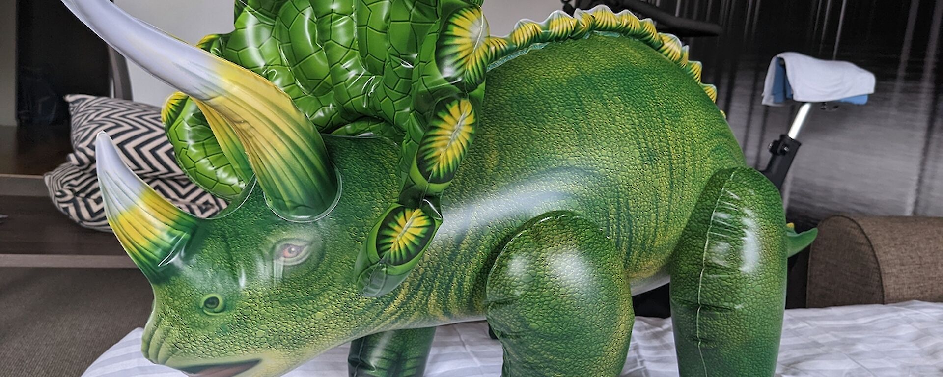 Inflatable triceratops toy stands on bed in hotel room