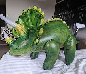 Inflatable triceratops toy stands on bed in hotel room