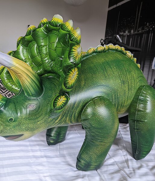 Inflatable triceratops toy stands on bed in hotel room