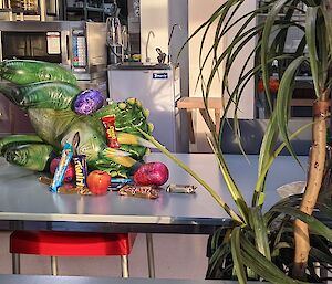 Inflatable triceratops toy lies on table in the mess surrounded by snacks