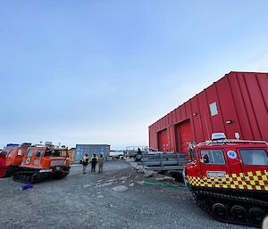 Two Hägglunds face to face connected by a winch rope with red workshop building behind