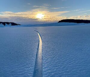 view across sea ice to rocky islands in the distance with crack in the sea ice running from photographer all the way towards the horizen