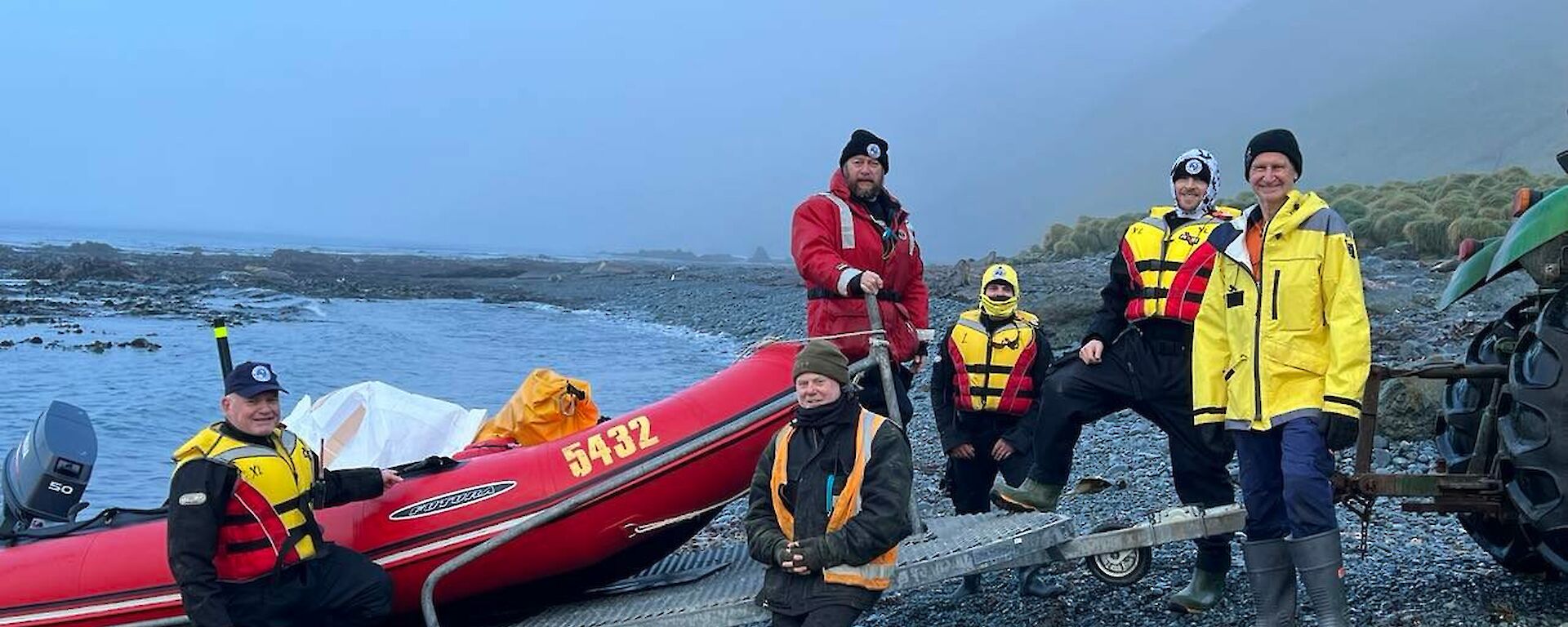 A crew in life jackets prepare to launch a boat from a grey gravelly beach