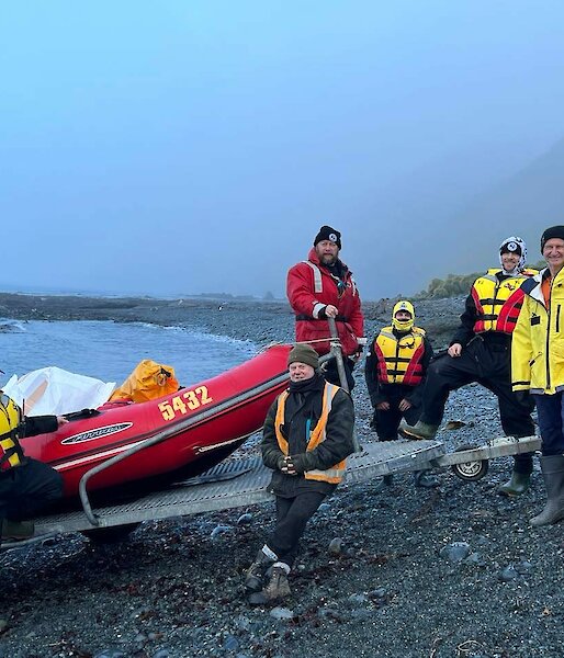A crew in life jackets prepare to launch a boat from a grey gravelly beach