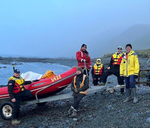 A crew in life jackets prepare to launch a boat from a grey gravelly beach