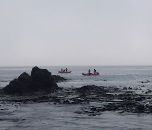 Two small boats float past a rocky outcrop