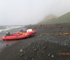 Two red boats sit on the shore with mist covered hills behind.