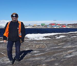 Man stands on rocky promontory with Mawson station behind in distance