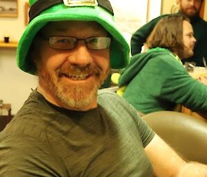 Close up of man sitting at bar wearing a bright green leprechaun's hat