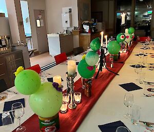 Long table set with tablecloths, candles, glassware, and centerpieces of green balloons made to look like cacti in pots